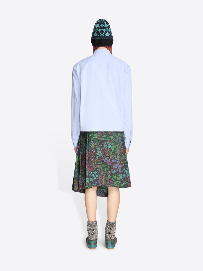 Back view of a person wearing a light blue shirt, patterned floral skirt, and green hat on a white background