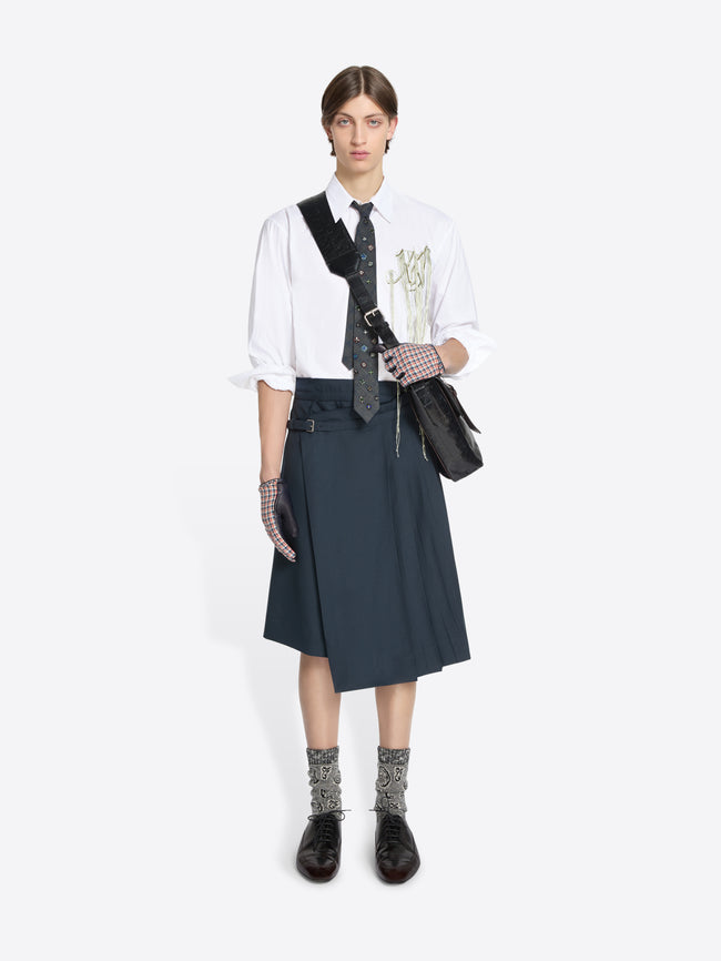 Person wearing a white shirt and skirt with a black bag on a white background