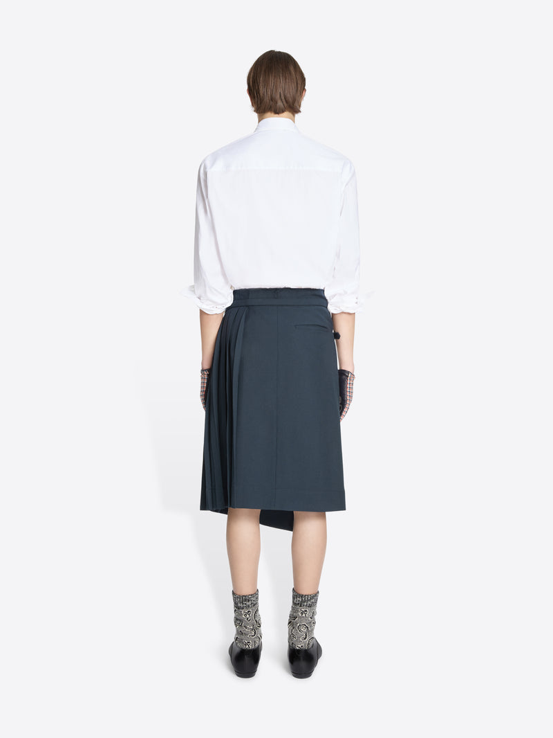 Back view of a person wearing a white shirt, dark skirt, patterned socks on a white background