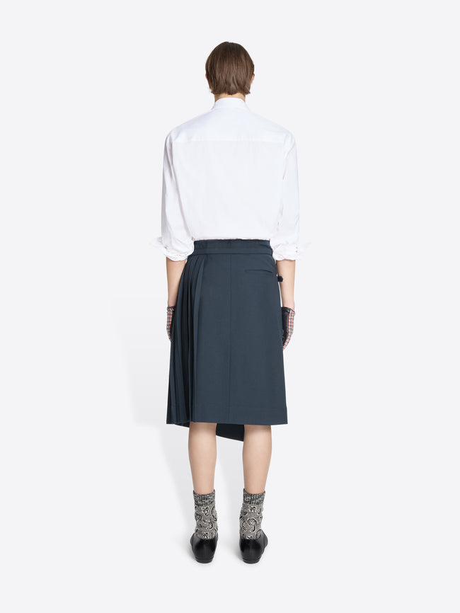 Back view of a person wearing a white shirt, dark skirt, patterned socks on a white background