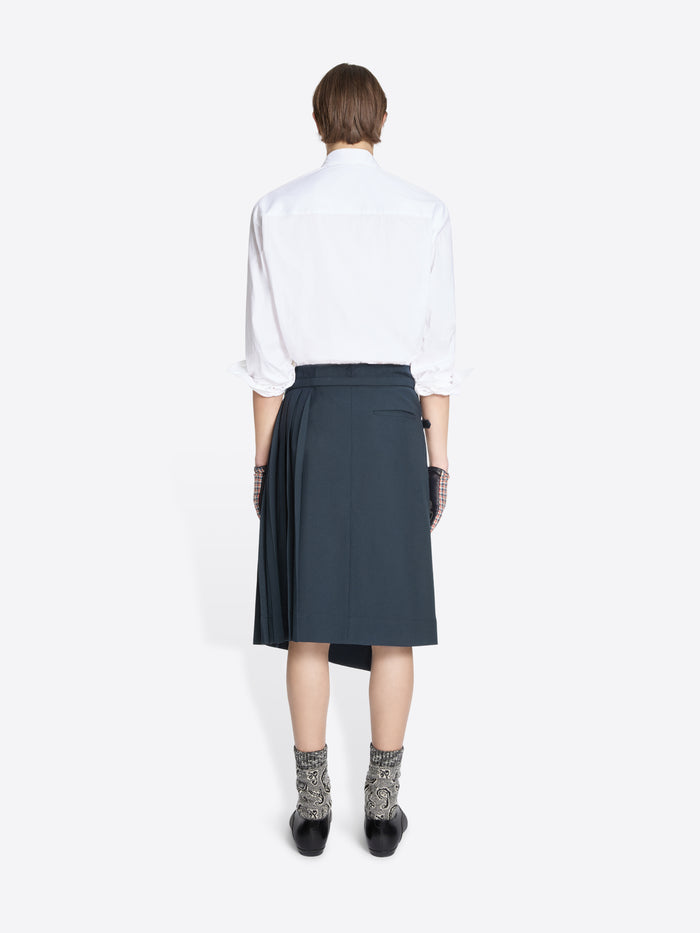 Back view of a person wearing a white shirt, dark skirt, patterned socks on a white background