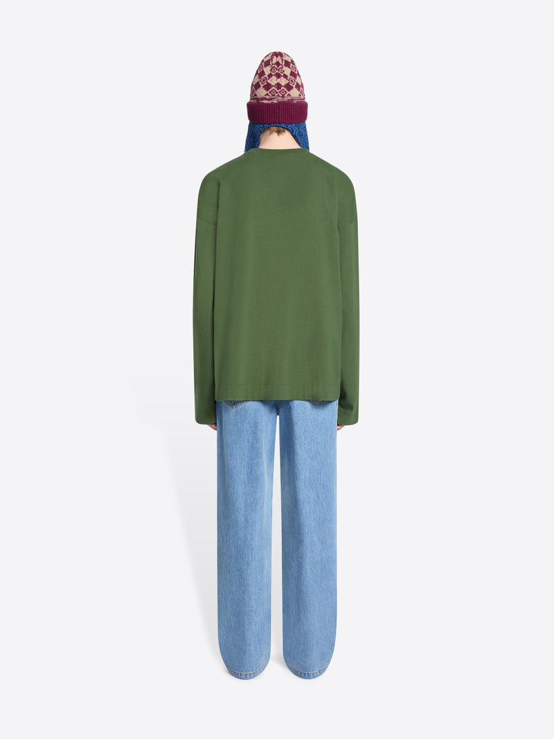 Person wearing a green sweater, blue jeans, and a colorful beanie holding a patterned bag on a white background