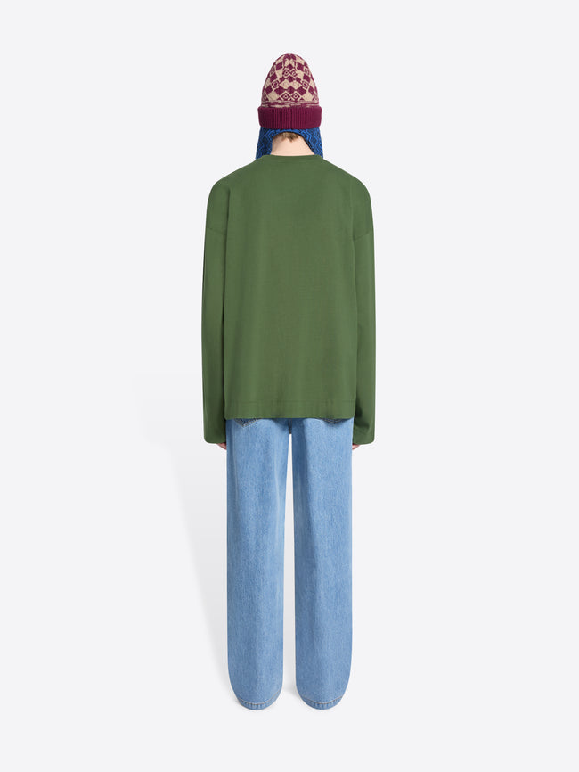 Person wearing a green sweater, blue jeans, and a colorful beanie holding a patterned bag on a white background