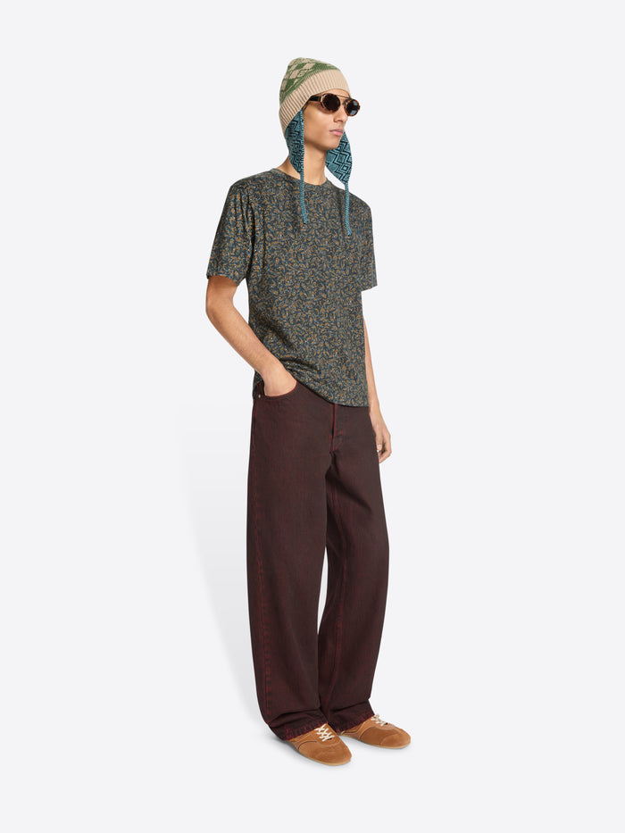 Person wearing a patterned t-shirt, red jeans, and a green hat with sunglasses on a white background