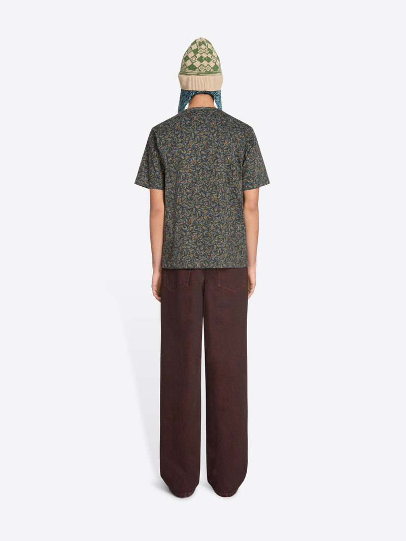 Back view of a person wearing a patterned t-shirt, red jeans, and a green hat on a white background