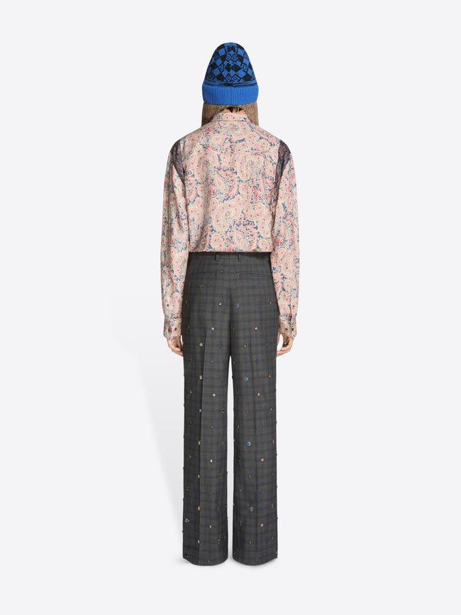 Back view of a person wearing a floral shirt and checkered pants with a blue beanie on a white background