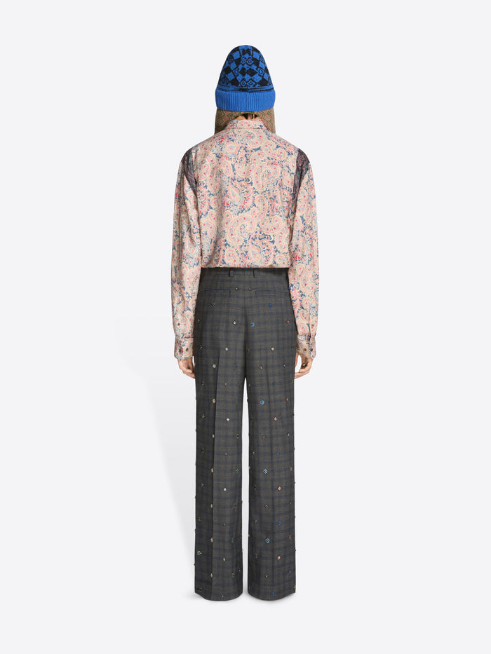 Back view of a person wearing a floral shirt and checkered pants with a blue beanie on a white background