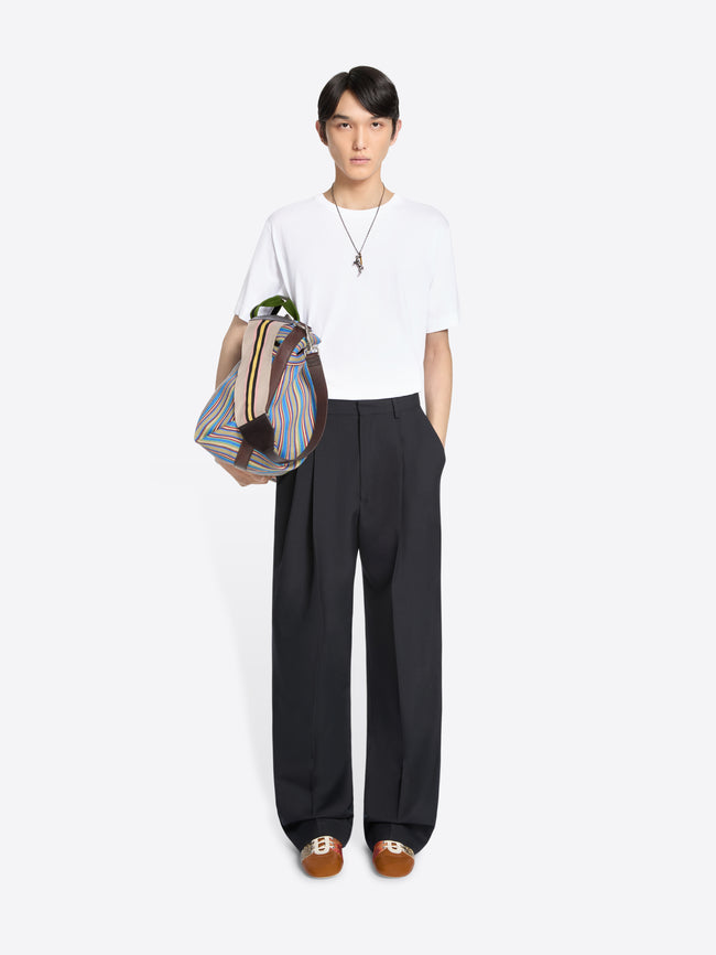 Person wearing a white t-shirt and black pants holding a colorful bag on a white background