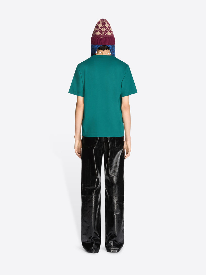 Person wearing a teal t-shirt and black pants with a patterned hat on a white background