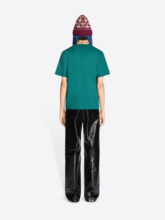 Person wearing a teal t-shirt and black pants with a patterned hat on a white background