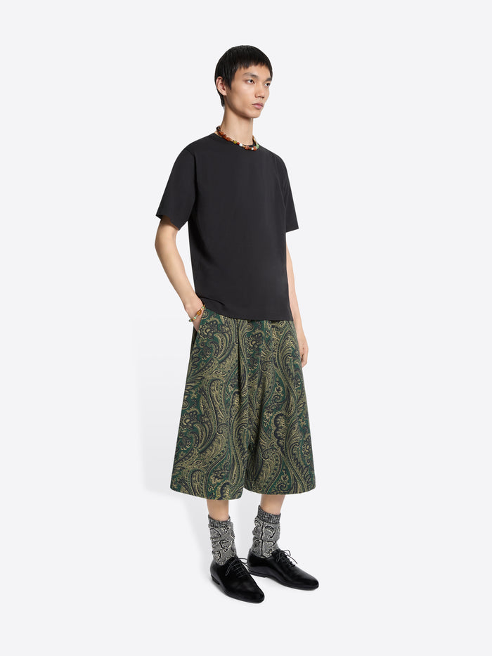 Person wearing a black t-shirt and green patterned shorts on a white background