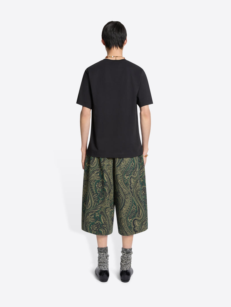Back view of a person wearing a black t-shirt and green patterned shorts on a white background