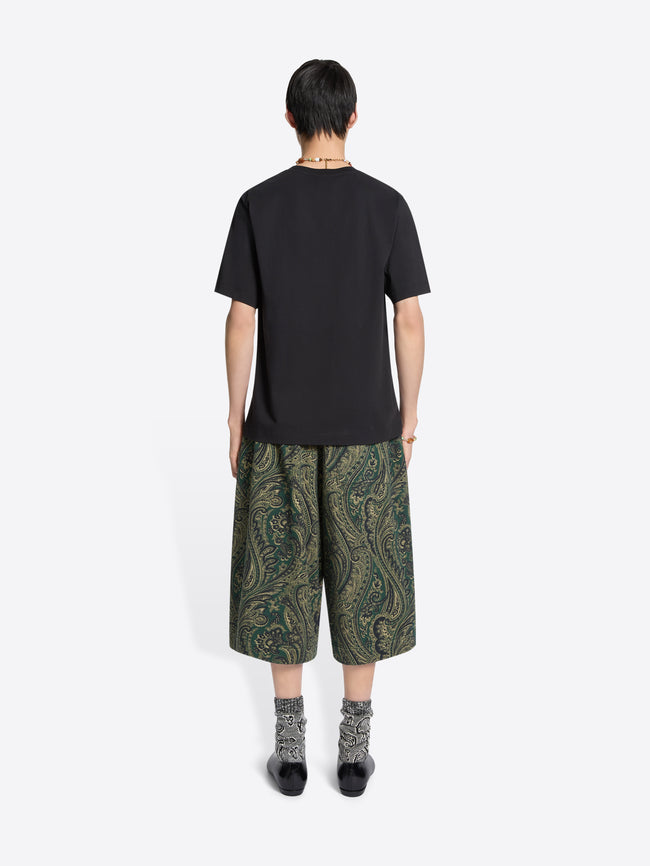 Back view of a person wearing a black t-shirt and green patterned shorts on a white background