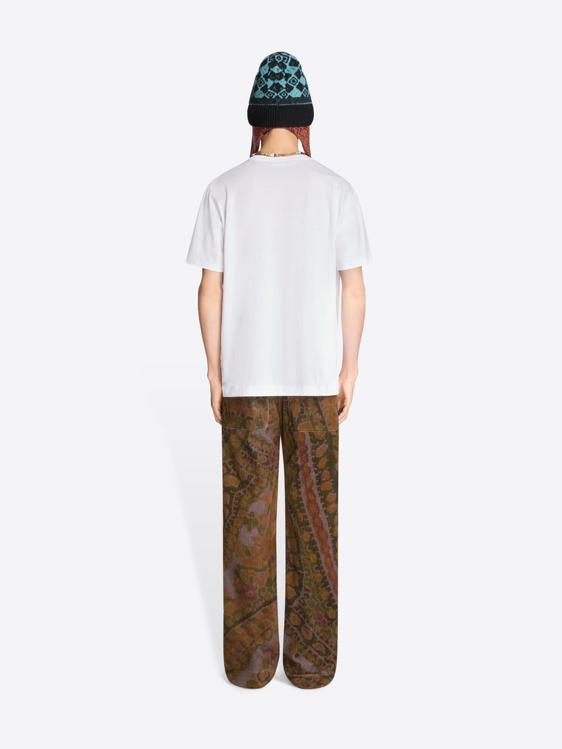 Back view of a person wearing a white t-shirt and patterned pants on a white background