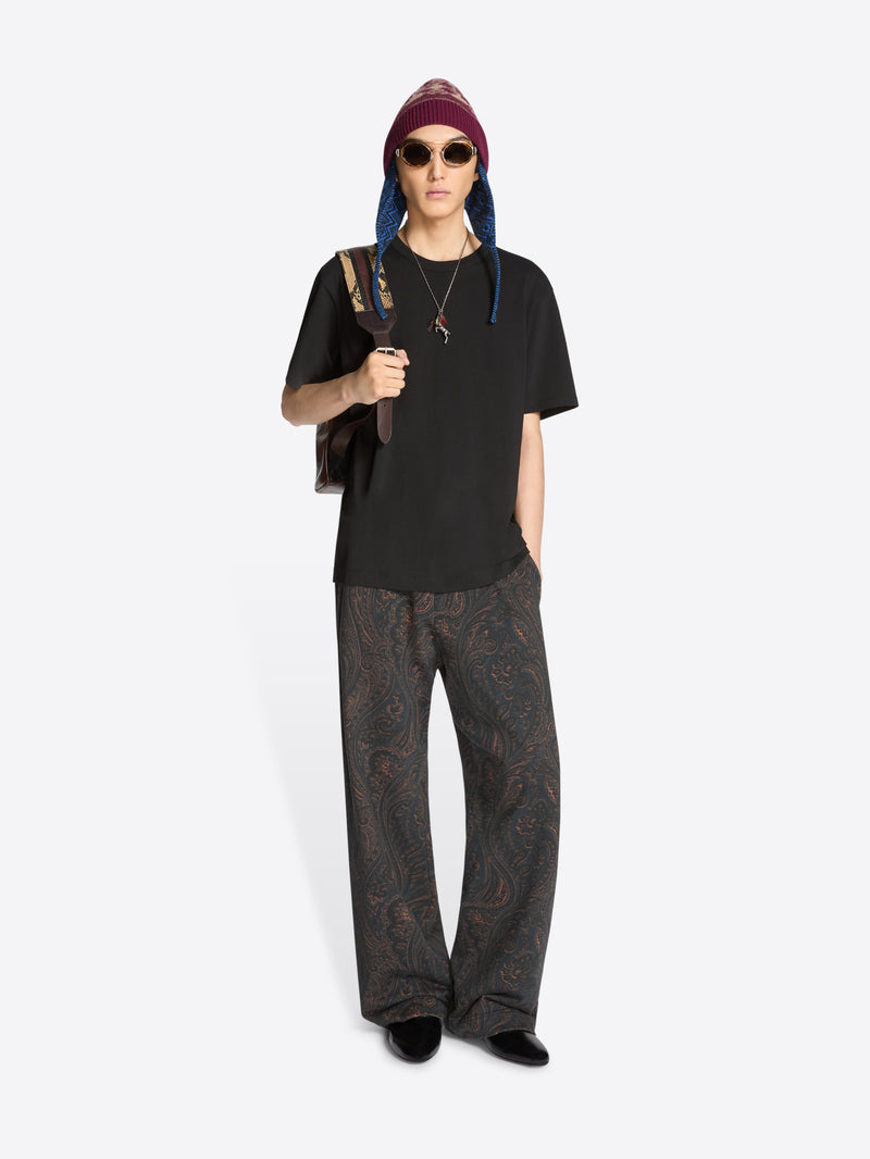 Person wearing a black t-shirt, patterned pants, and a beanie with sunglasses on a white background