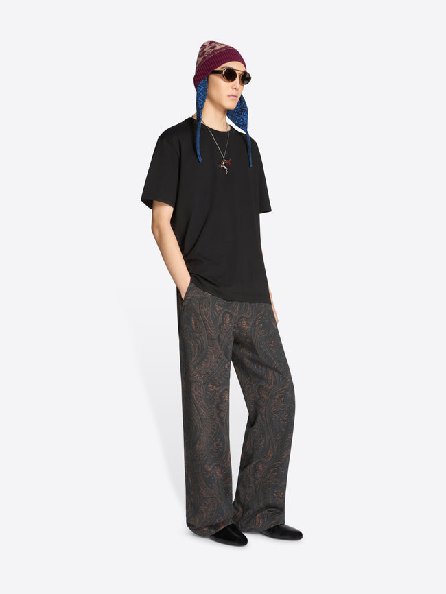 Person wearing a black t-shirt, patterned pants, and a colorful beanie on a white background