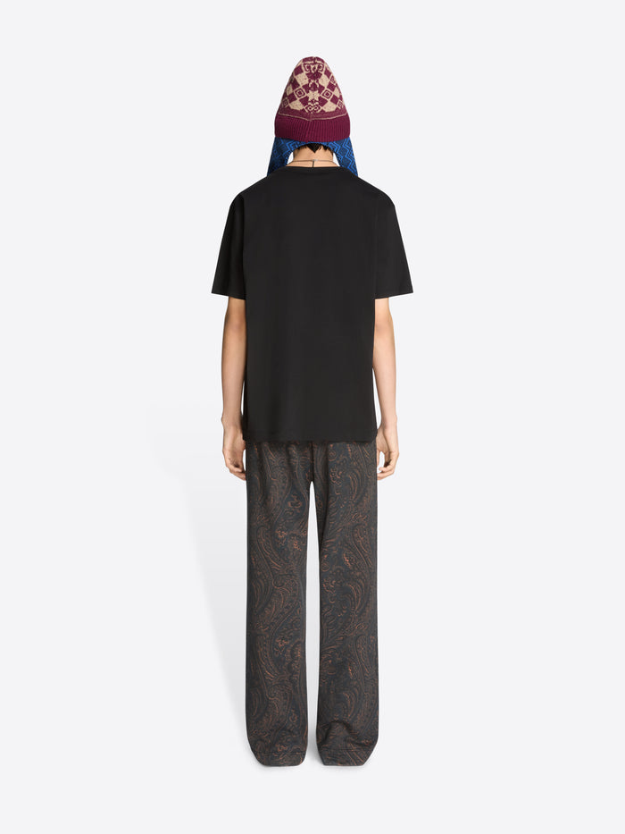 Back view of a person wearing a black t-shirt and patterned pants on a white background