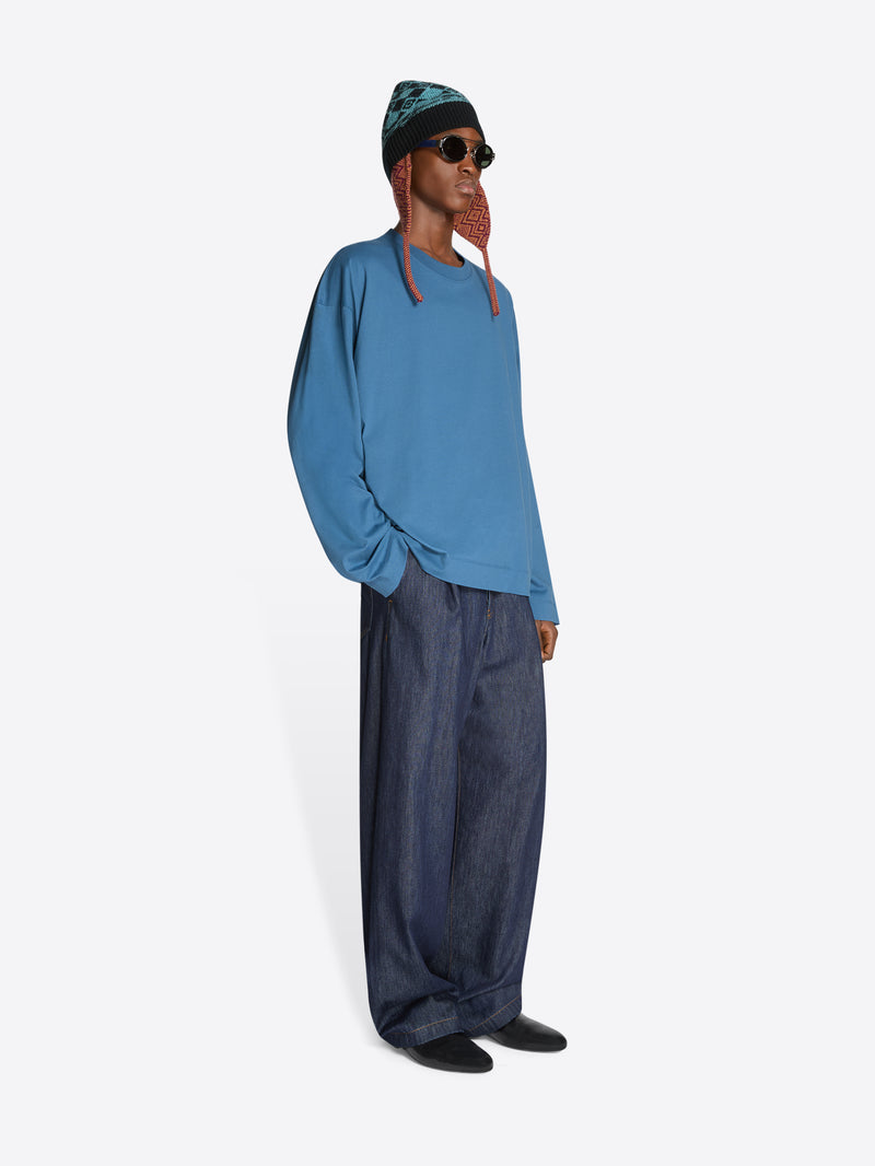 Person wearing a blue sweatshirt and dark jeans on a white background