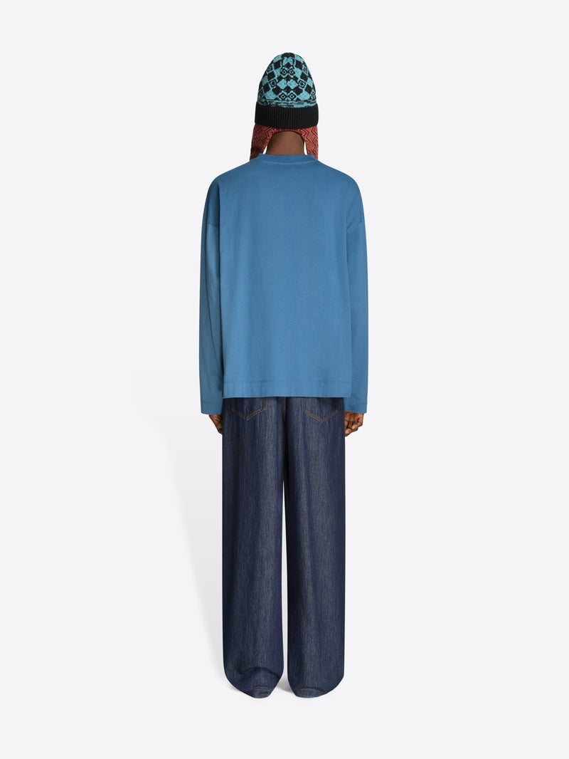 Back view of a person wearing a blue sweatshirt and dark pants with a patterned beanie on a white background