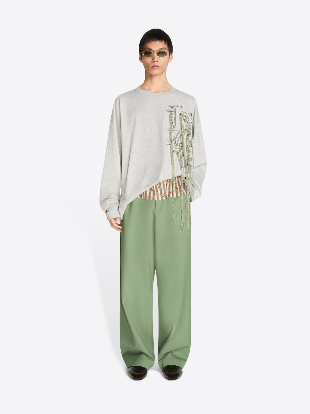Person wearing a light-colored sweatshirt and green pants on a white background