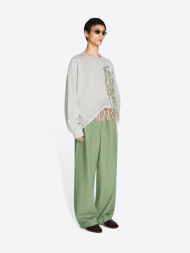 Person wearing a light gray sweater with text and green pants on a white background