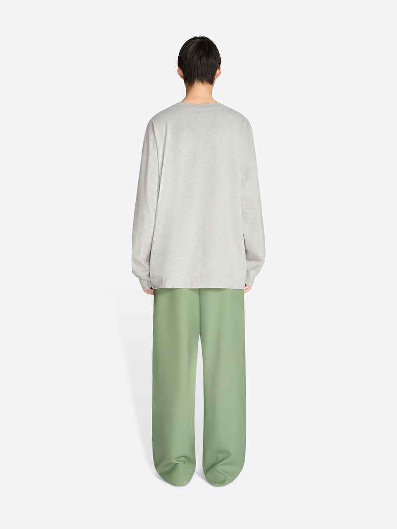 Person wearing a light gray sweater and green pants on a white background