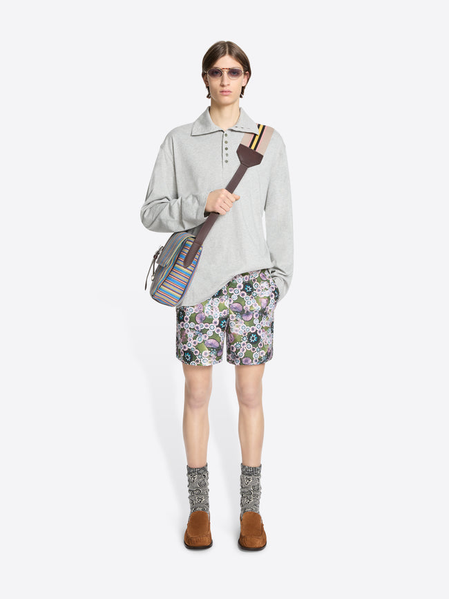 Person wearing a light gray turtleneck tee, floral shorts, holding a bag on a white background