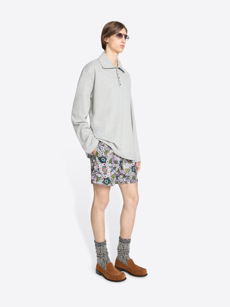 Person wearing a light gray turtleneck tee, patterned shorts, and brown shoes on a white background