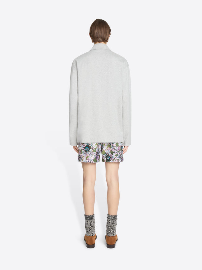 Back view of a person wearing a light gray turtleneck tee, floral shorts, and patterned socks on a white background