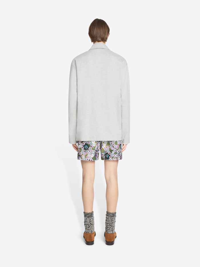 Back view of a person wearing a light gray turtleneck tee, floral shorts, and patterned socks on a white background
