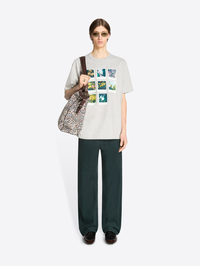 Person wearing a graphic t-shirt and dark pants with a patterned bag on a white background