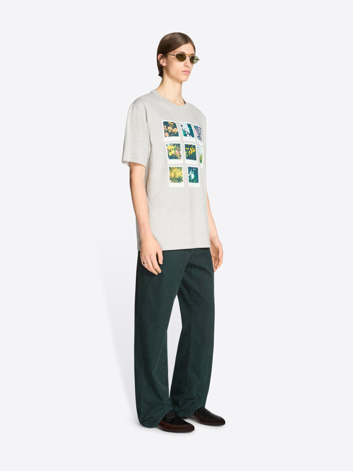 Person wearing a light-colored t-shirt with graphic design and dark green pants on a white background