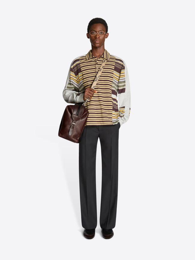 Person wearing a striped polo and holding a brown bag on a white background