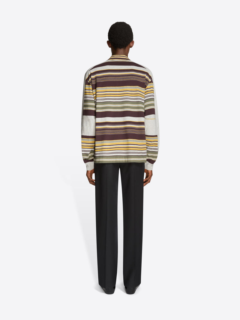 Back view of a person wearing a striped polo and black pants on a light gray background