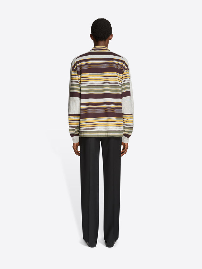 Back view of a person wearing a striped polo and black pants on a light gray background
