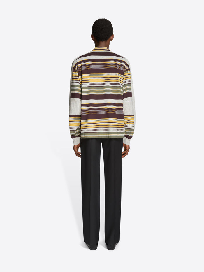 Back view of a person wearing a striped polo and black pants on a light gray background