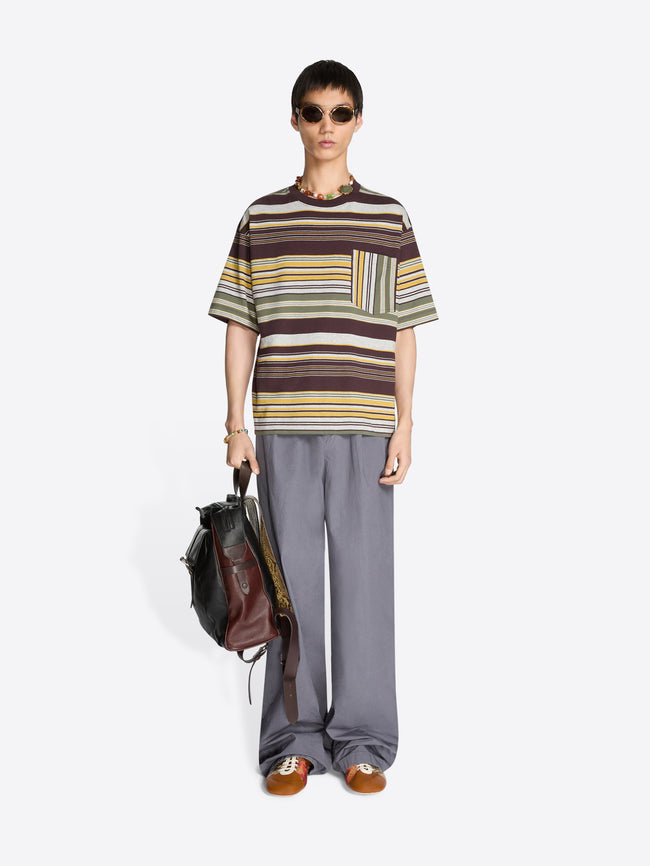 Person wearing a striped t-shirt and gray pants holding a backpack on a white background