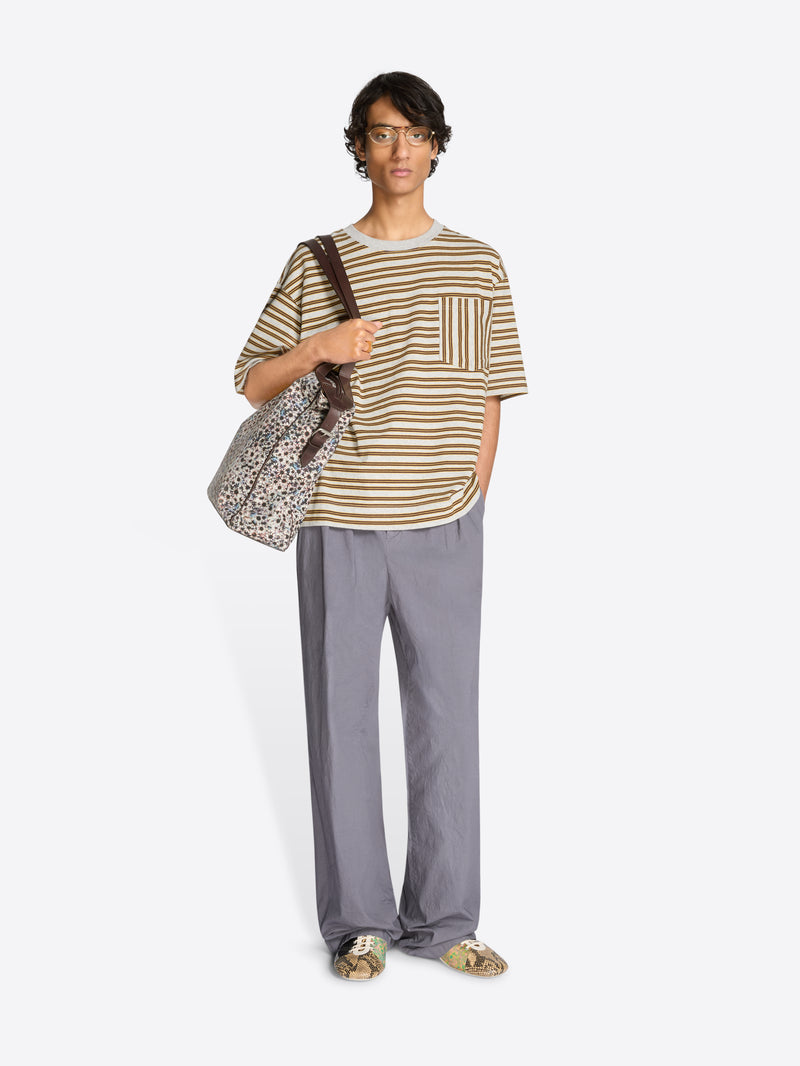 Person wearing a striped t-shirt and gray pants holding a patterned bag on a white background