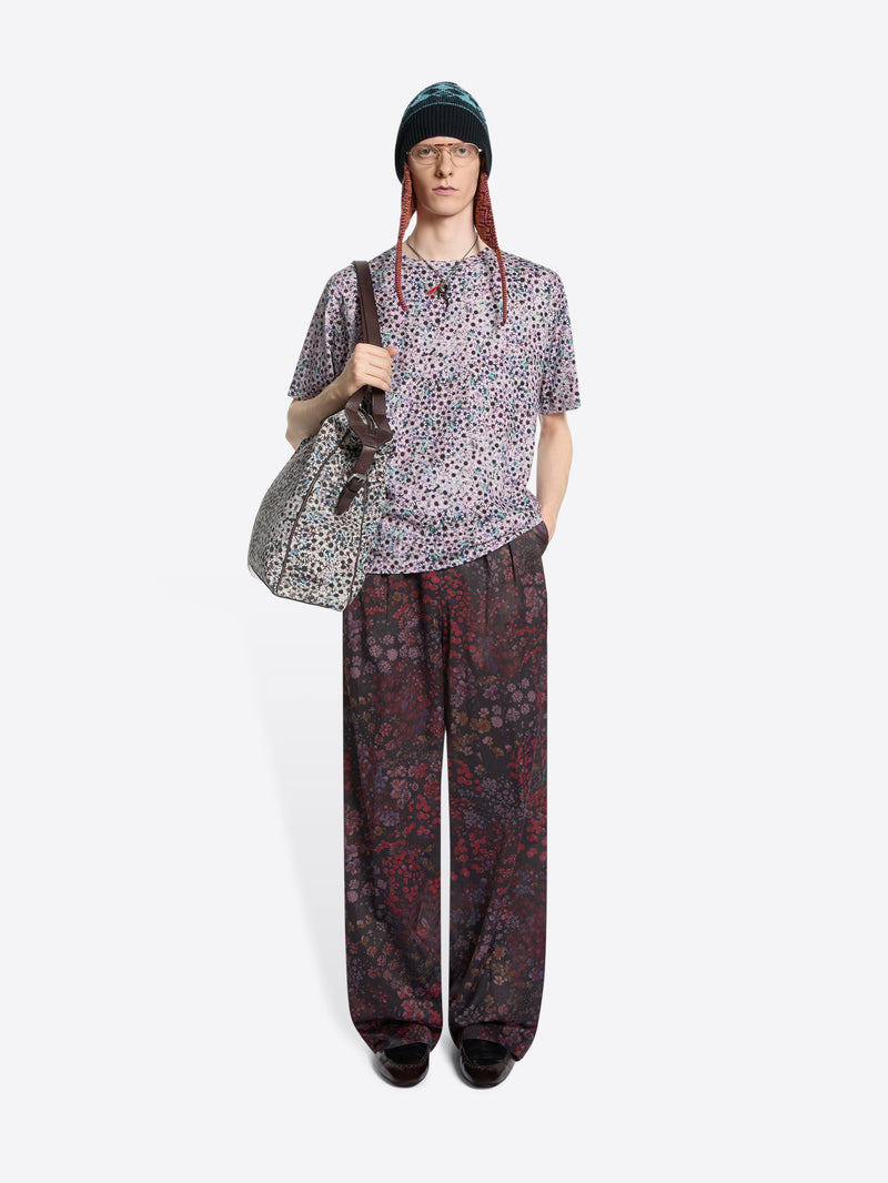 Person wearing a patterned t-shirt and pants with a bag on a white background