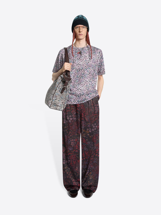Person wearing a patterned t-shirt and pants with a bag on a white background