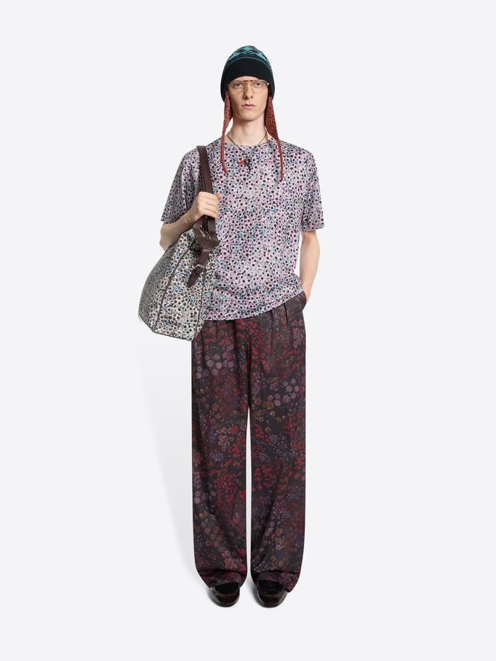 Person wearing a patterned t-shirt and pants with a bag on a white background