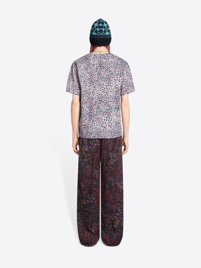Person wearing a patterned t-shirt and pants with a bag on a white background