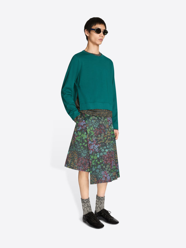 Person wearing a teal sweater and patterned skirt on a white background