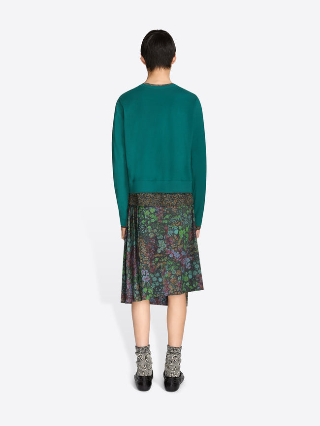 Back view of a person wearing a teal sweater and patterned skirt on a white background