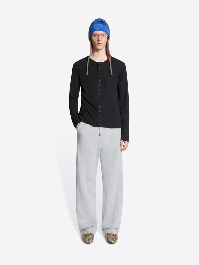 Person wearing a black cardigan, gray sweatpants, and a blue hat on a white background
