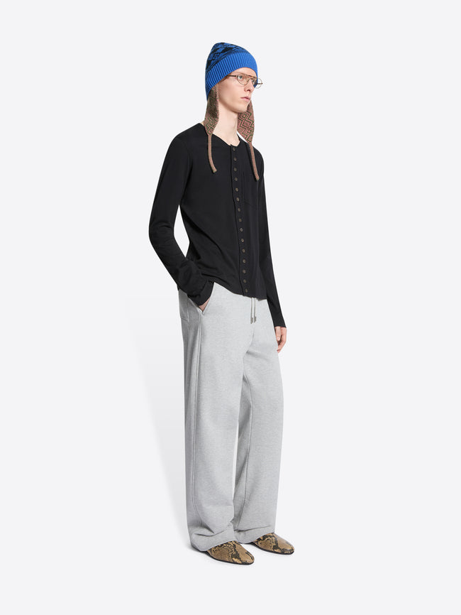 Person wearing a black cardigan, gray sweatpants, and a blue hat on a white background