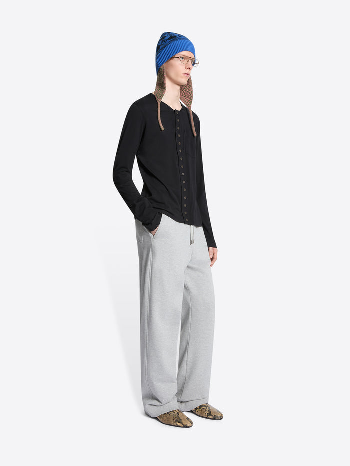 Person wearing a black cardigan, gray sweatpants, and a blue hat on a white background
