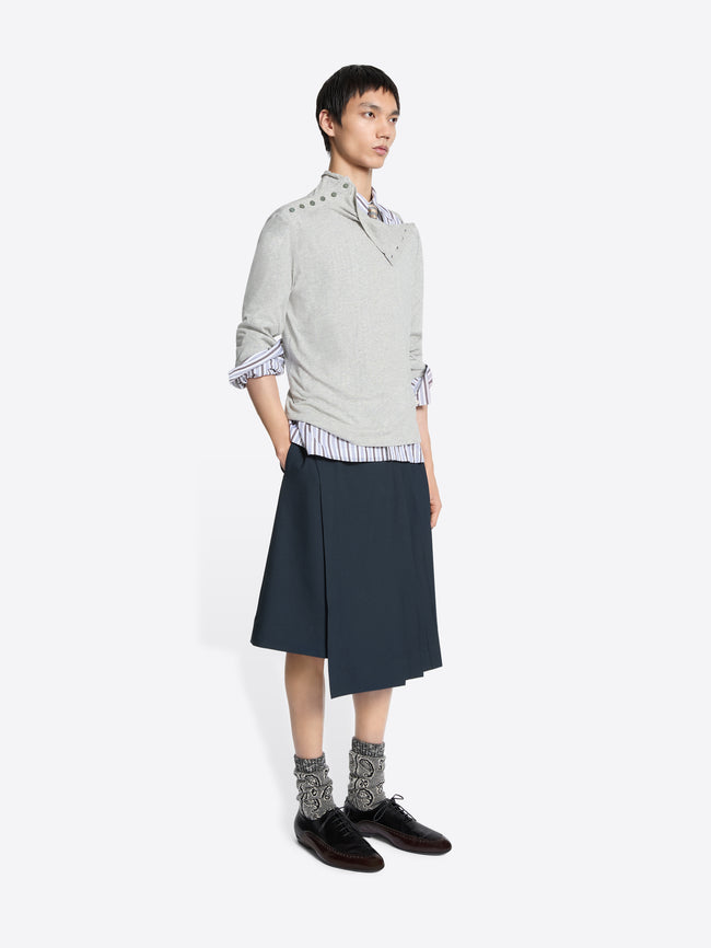 Person wearing a light gray sweater, striped shirt, dark blue skirt, and patterned socks on a white background