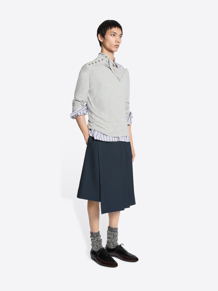 Person wearing a light gray sweater, striped shirt, dark blue skirt, and patterned socks on a white background