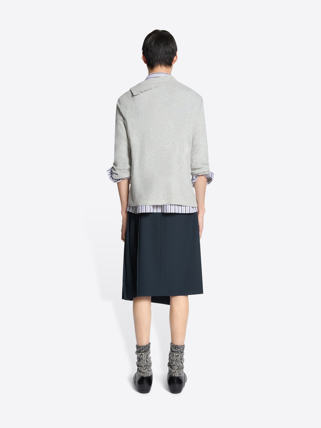 Person wearing a light gray sweater, striped shirt, dark blue skirt, and patterned socks on a white background